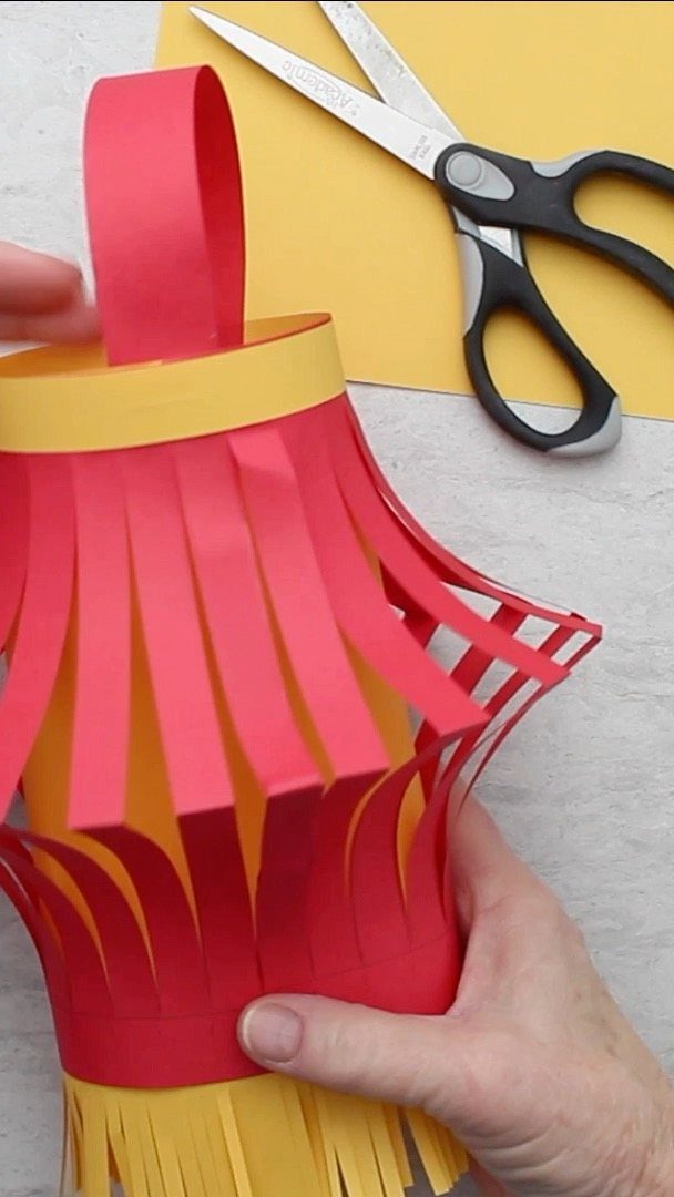 Handmade red and yellow paper lantern held by hands next to scissors.