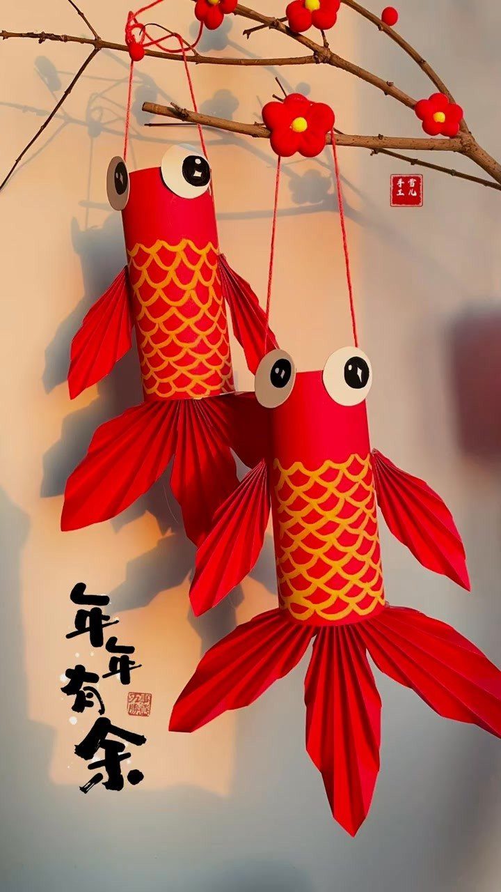 Red paper fish ornaments with yellow scales hanging from a flowering branch