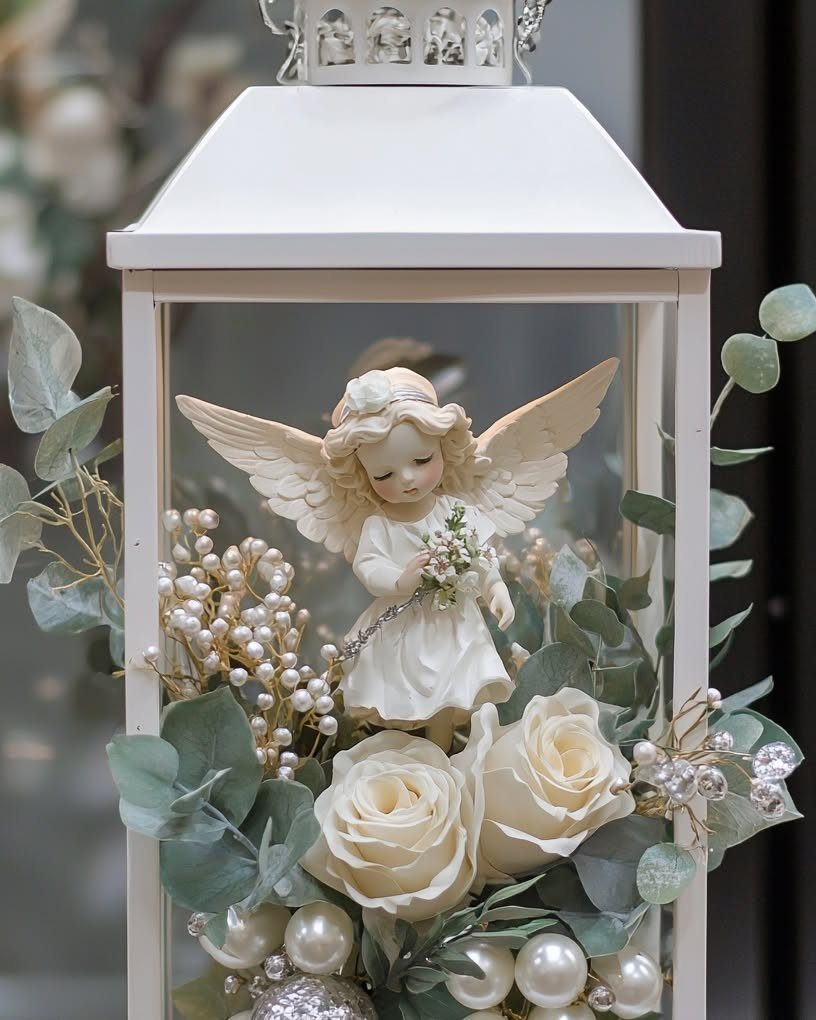 White decorative lantern filled with an angel figurine, white roses, and pearls.