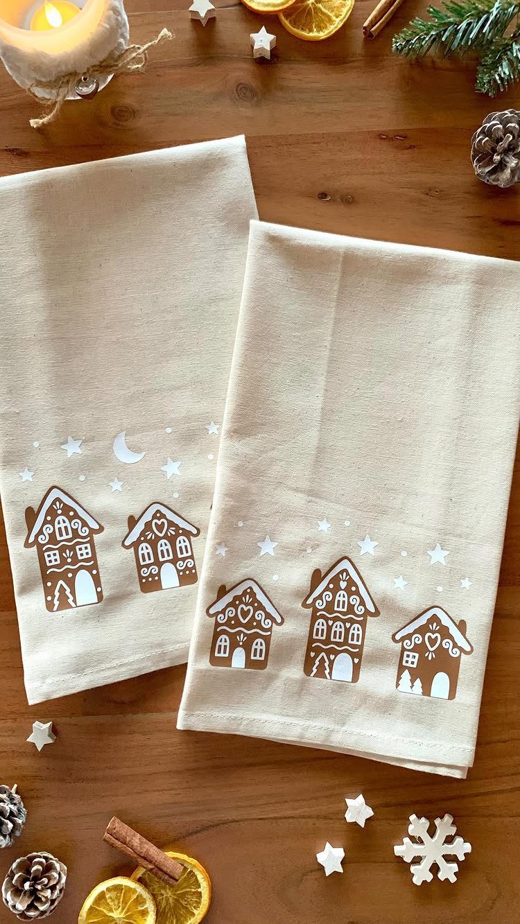 Beige tea towels with stamped gingerbread house designs on a wooden table.