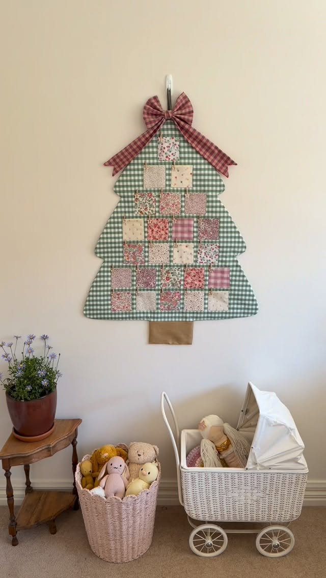Fabric Christmas tree wall hanging with patterned pockets and a red plaid bow.