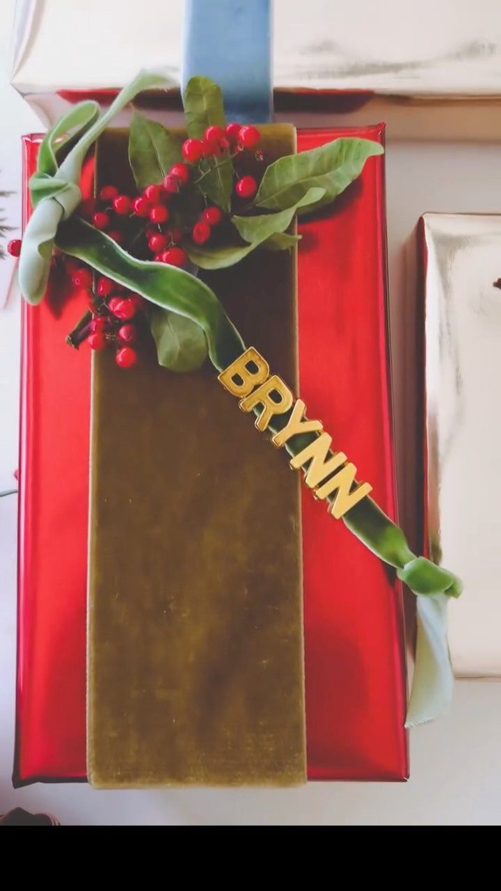 Red wrapped gift with green velvet ribbon, red berries, and gold name tag