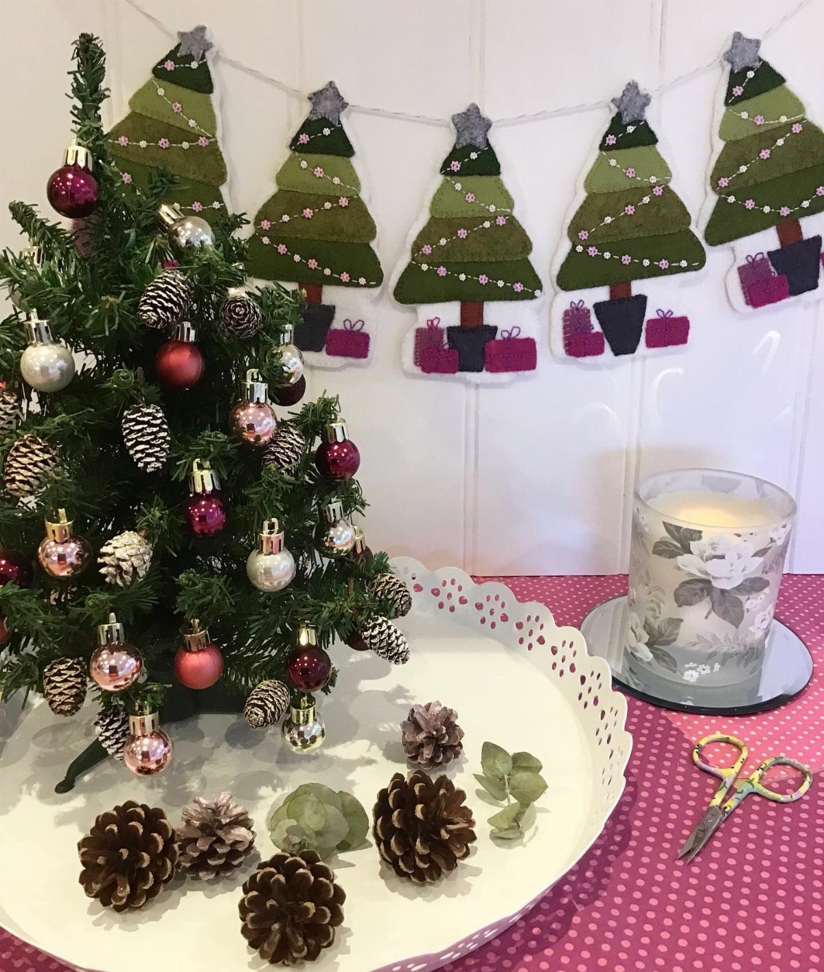 Felt Christmas tree garland hanging behind a small decorated tree and pinecones.
