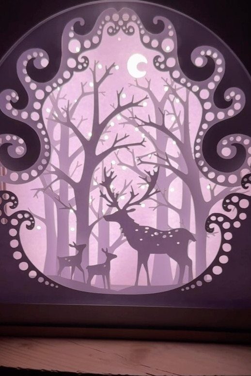 Glowing purple shadow box with paper cutouts of deer in a winter forest
