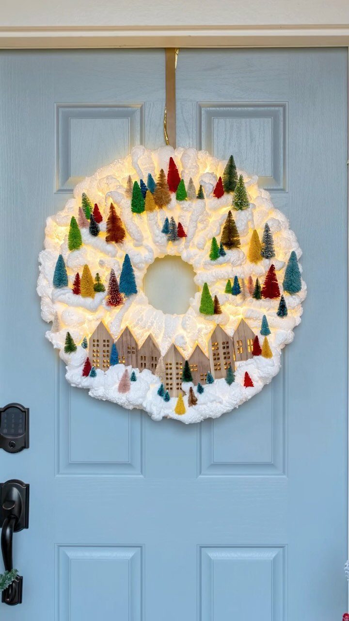 White snowball wreath with miniature trees and houses hanging on a blue door