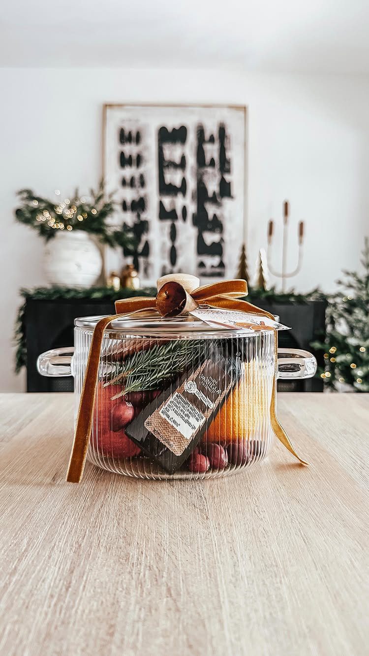 Glass pot filled with cinnamon, oranges, and cranberries tied with a brown ribbon.