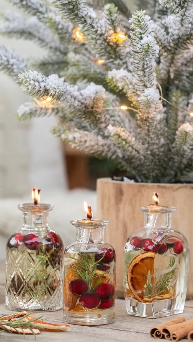 Three lit holiday candles in glass jars with cranberries and orange slices.