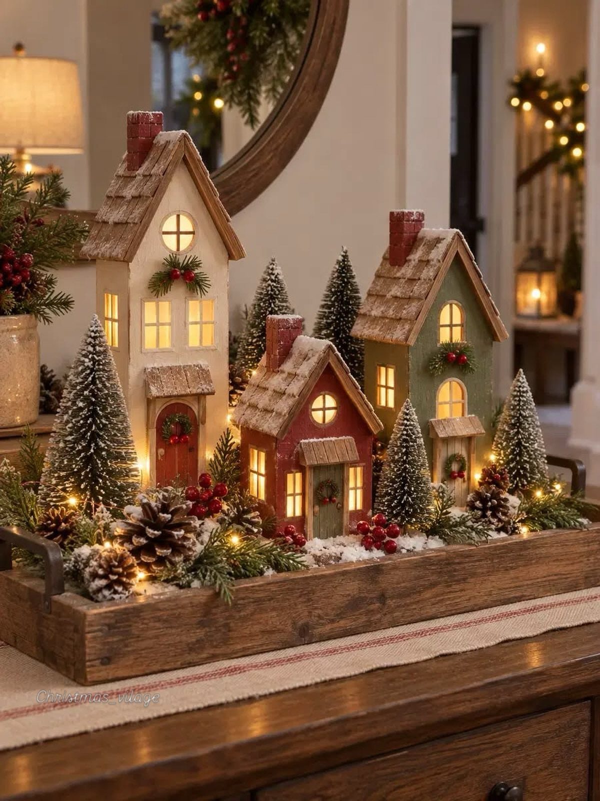 Miniature winter village with glowing houses and frosted trees in a wooden tray.