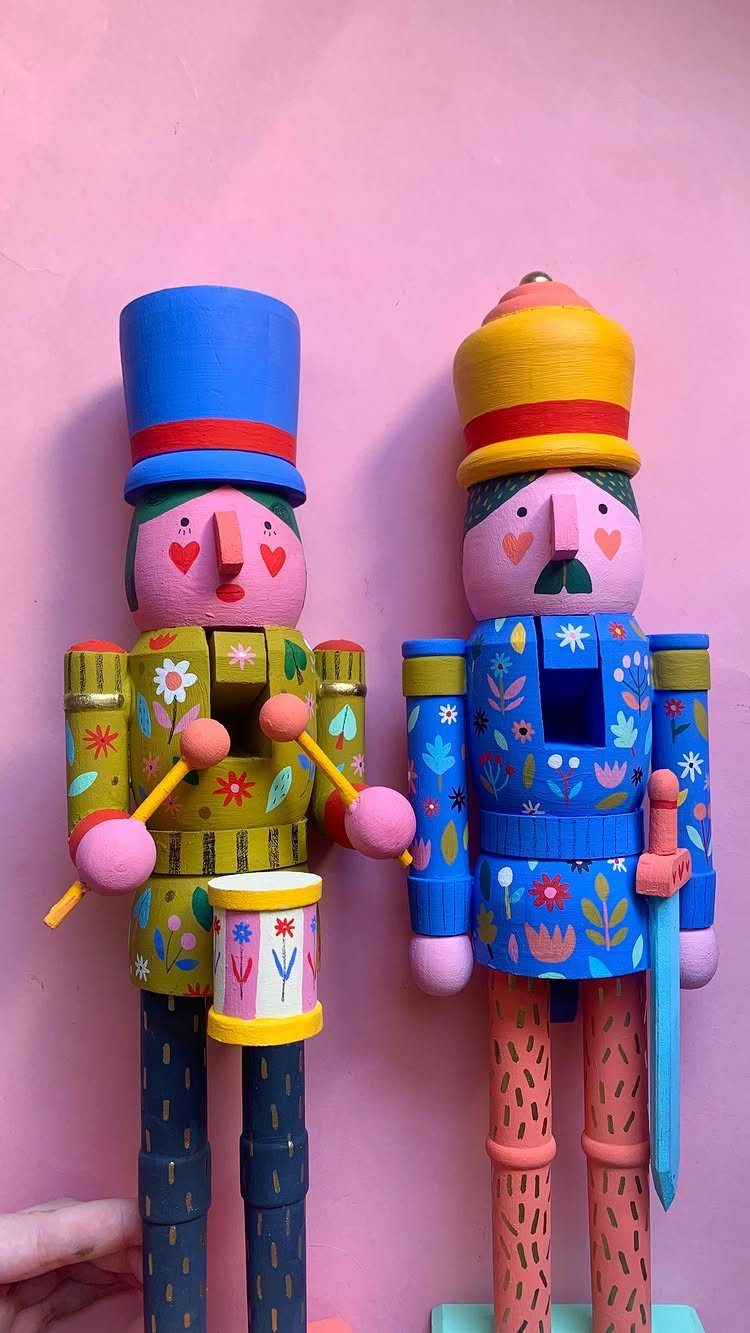 Two colorful hand-painted wooden nutcrackers with floral patterns against a pink background.