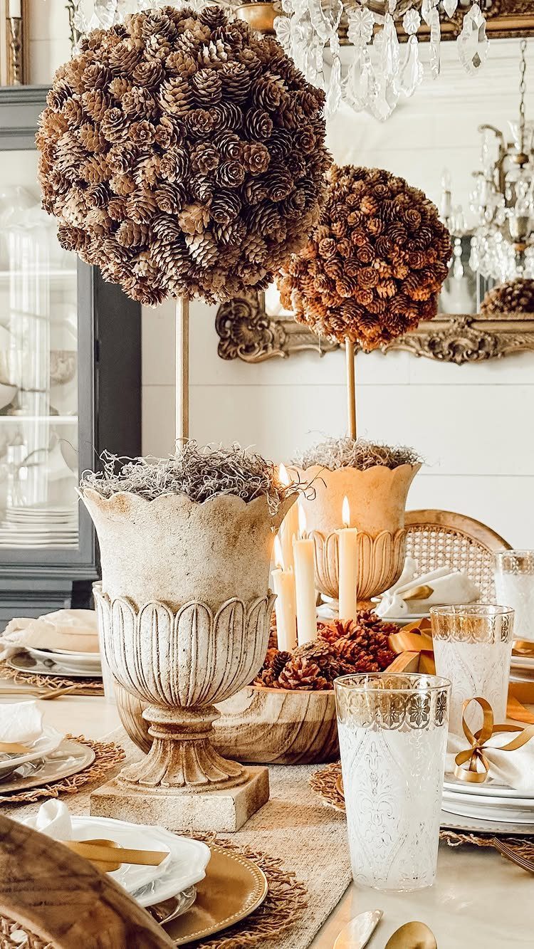 Two pinecone topiaries in ornate urns on a decorated holiday dining table.