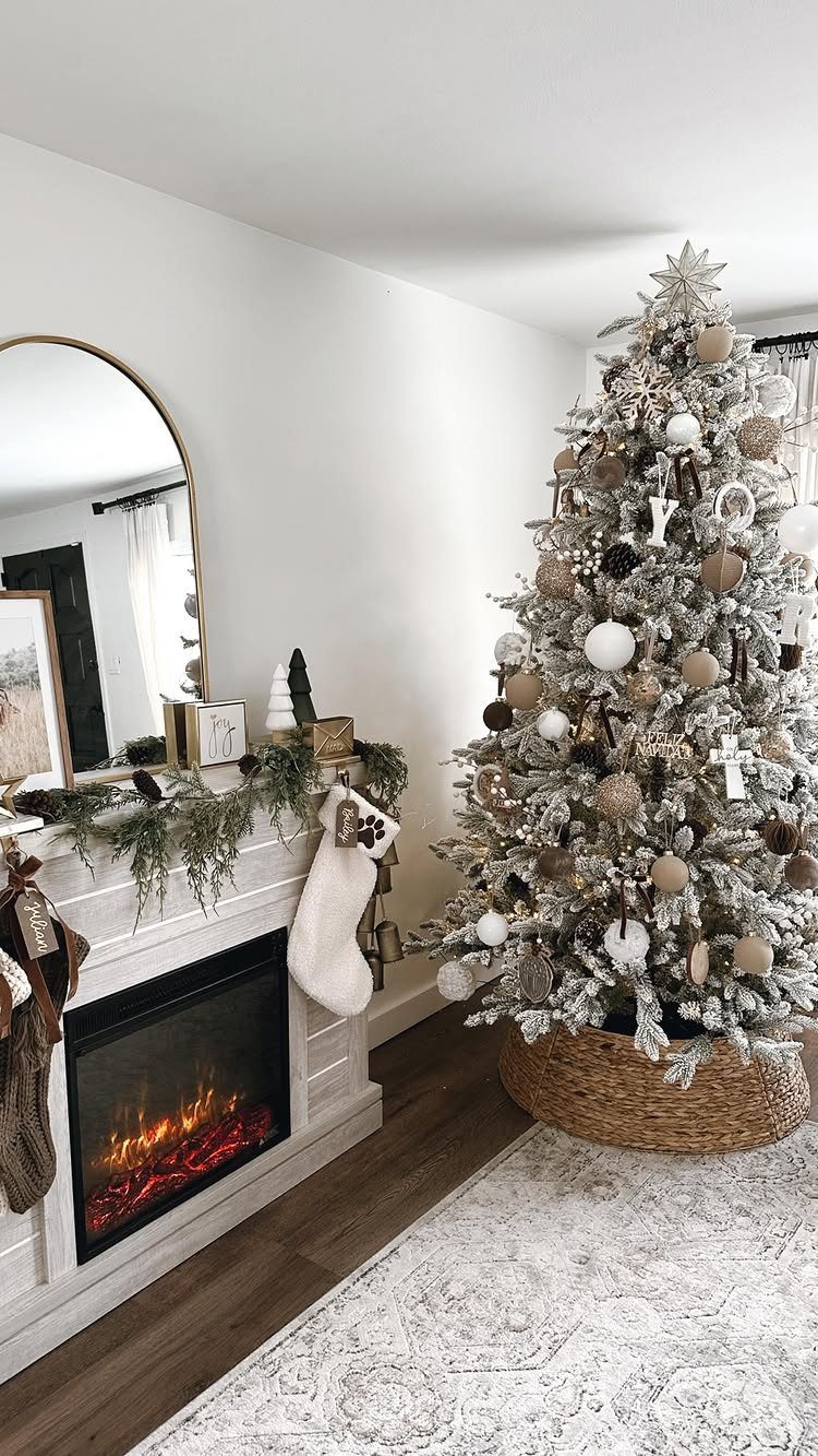 Flocked Christmas tree with metallic ornaments beside a white fireplace with festive greenery.