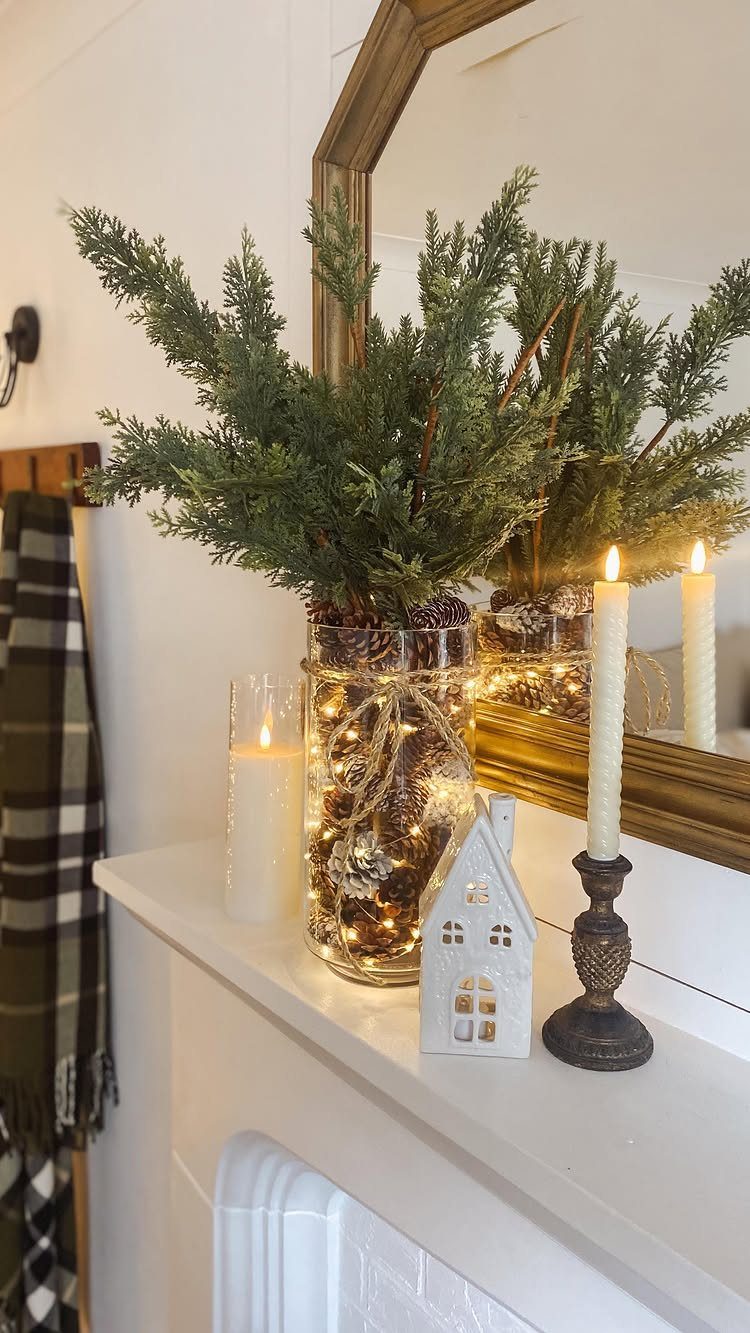 Evergreen branches in a glass vase with fairy lights on a white mantel.