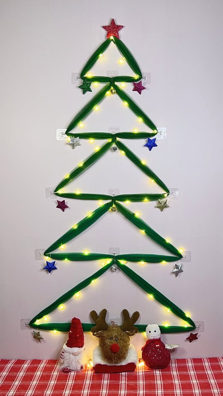 Wall Christmas tree made from green fabric and lights with colorful star ornaments.