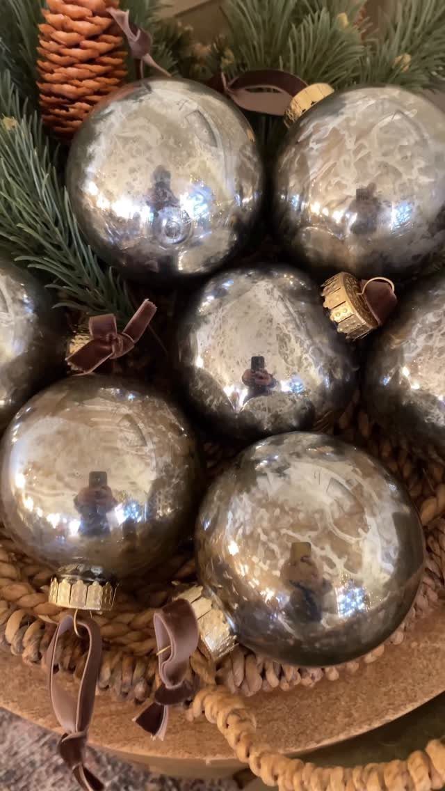 Silver mercury glass ornaments in a woven basket with pine needles and pinecones.