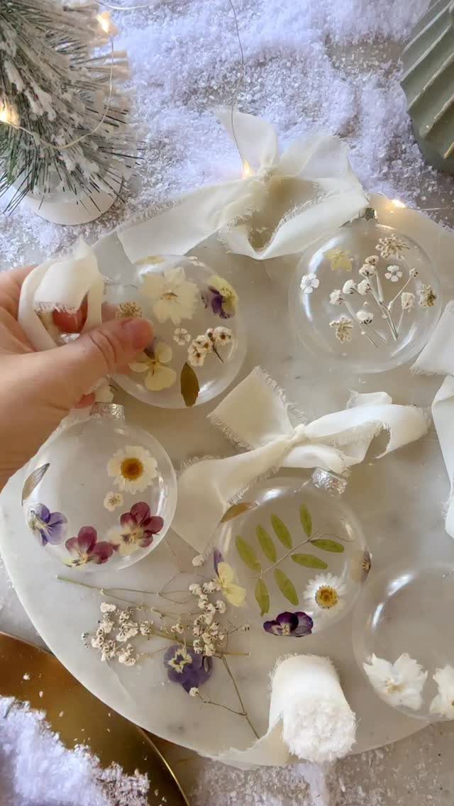 Clear glass Christmas ornaments with dried flowers on a marble tray with snow