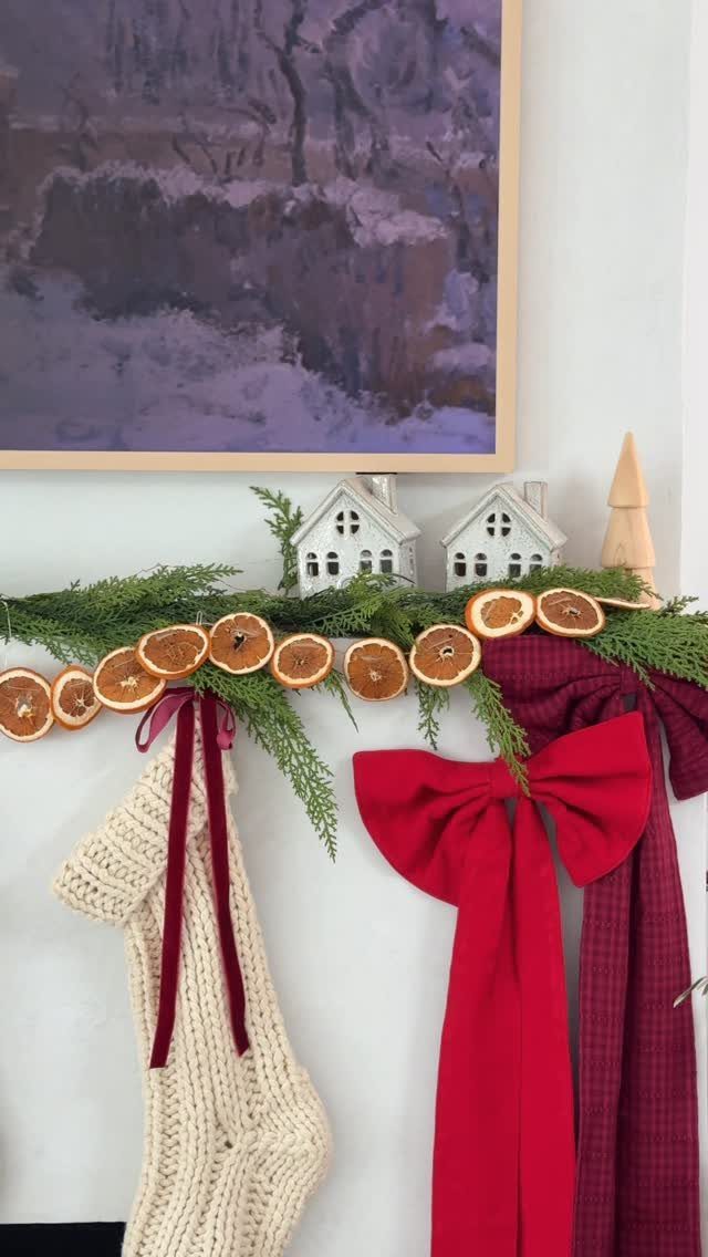 Dried orange slices on a green evergreen garland with a red bow and stocking.