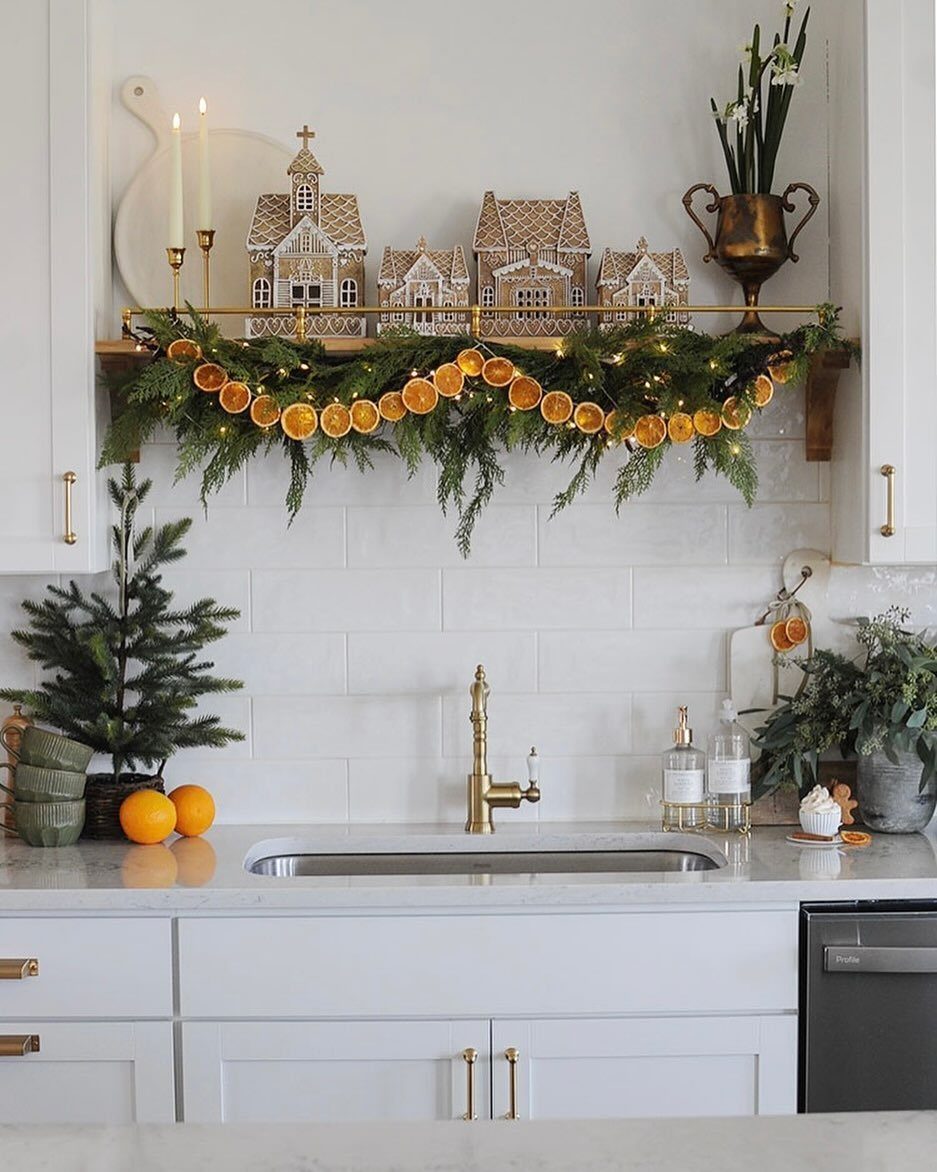 Gingerbread houses and orange slice garlands decorating a white kitchen shelf