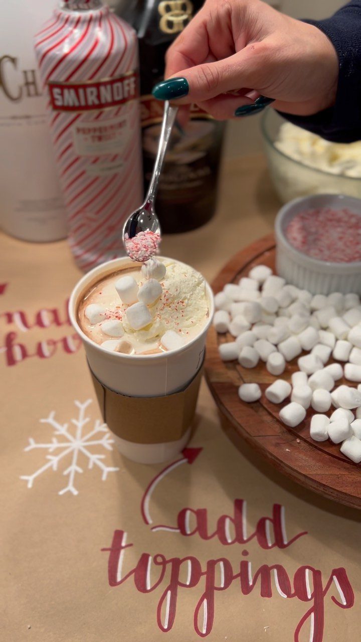 Hand adding pink sprinkles to hot cocoa with marshmallows at a topping station