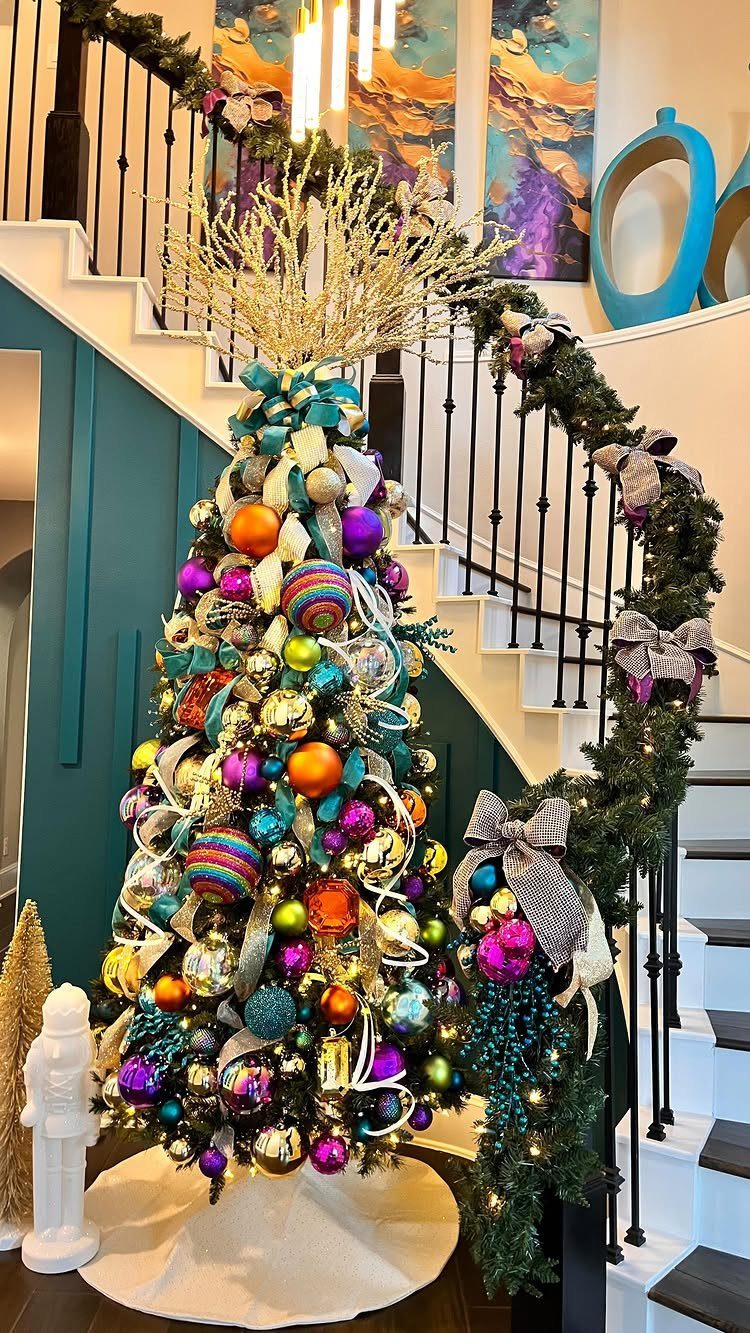 Decorated Christmas tree with teal, purple, and gold ornaments beside a staircase garland.