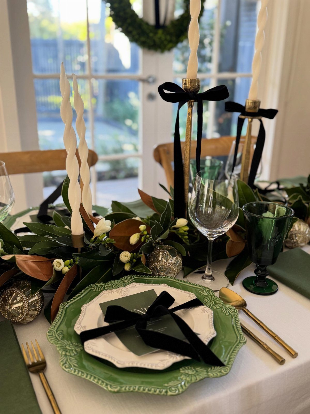 Formal table setting with green plates, gold cutlery, and Christmas ornaments in greenery.