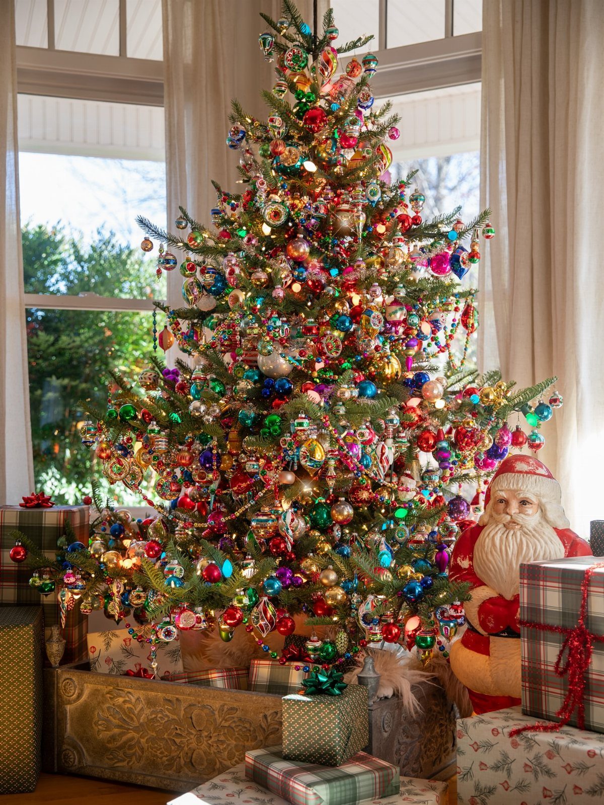 Decorated Christmas tree with multicolored vintage ornaments, Santa figure, and wrapped gifts.