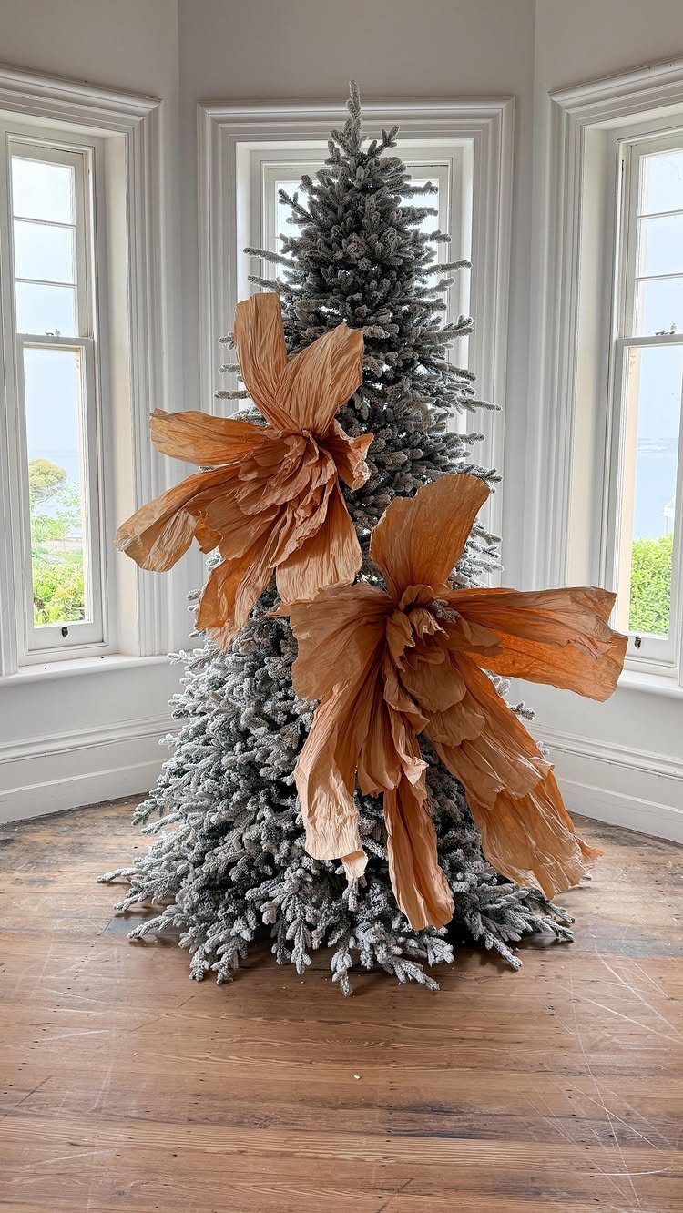 Flocked white Christmas tree decorated with large, orange-brown fabric floral blooms.