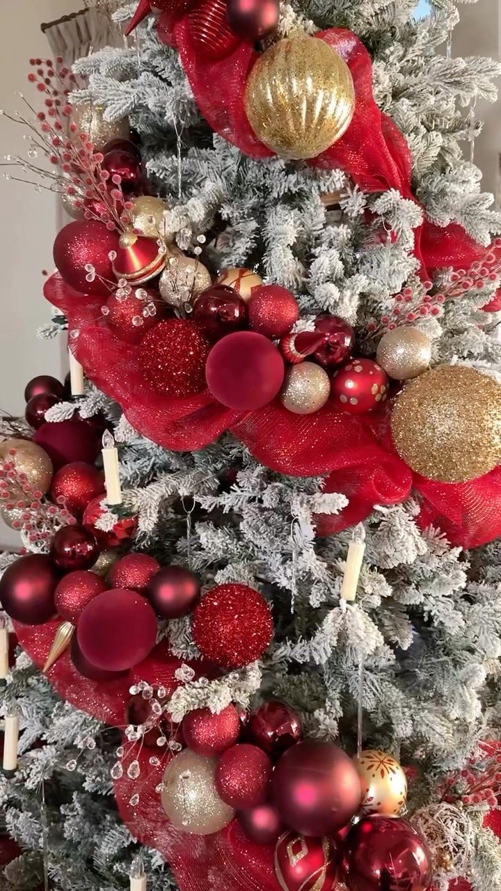 Flocked Christmas tree decorated with red and gold ornaments and red mesh ribbon.