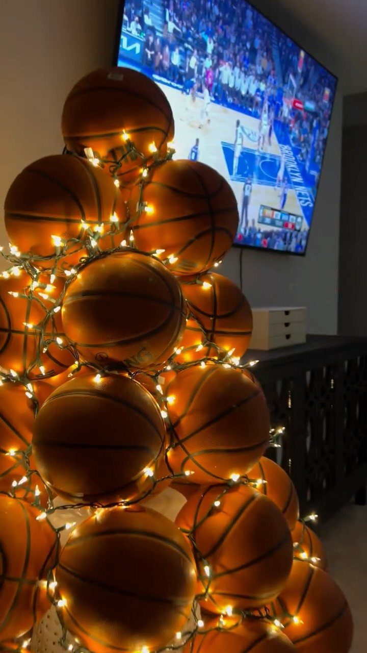 Basketballs stacked in a tree shape wrapped in warm white fairy lights.
