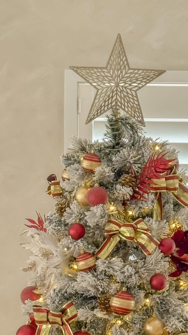 Flocked Christmas tree topped with a large gold wire star and red ornaments.