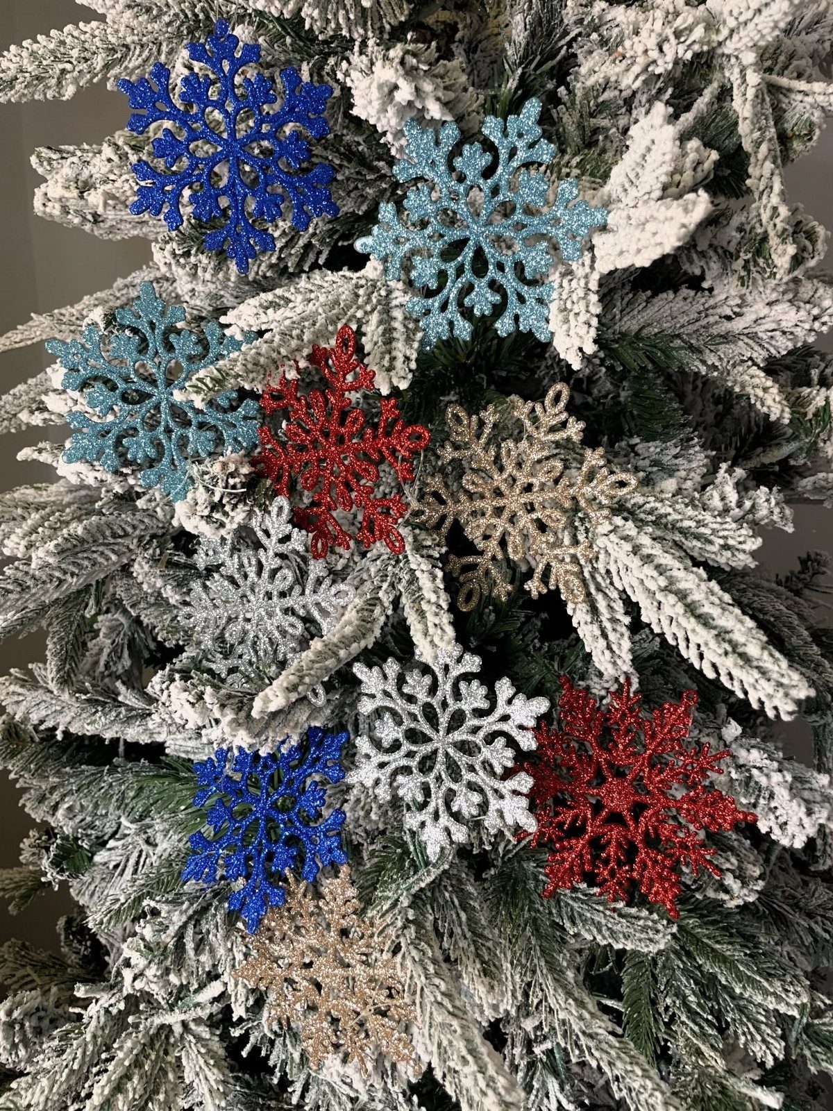 Glittery snowflake ornaments in various colors hanging on a snow-covered Christmas tree
