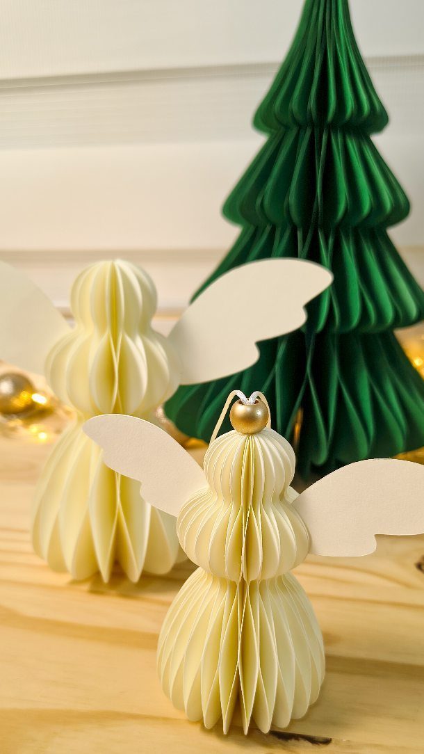 White pleated paper angel ornaments standing before a green pleated paper Christmas tree.