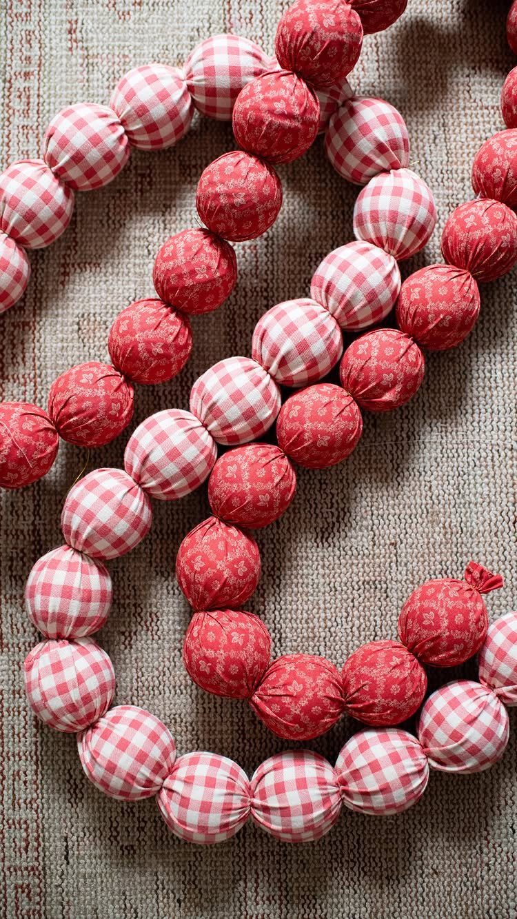 Red and gingham fabric ornaments strung together on a textured beige background.