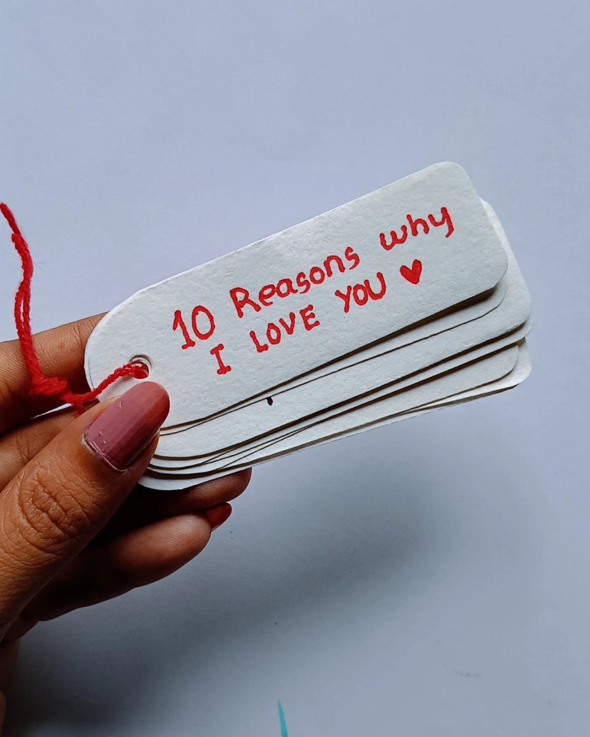 Hand holding a stack of handmade white tags saying 10 Reasons why I Love You