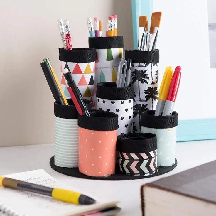 Desk organizer made from patterned cylindrical tubes holding various pens and pencils.