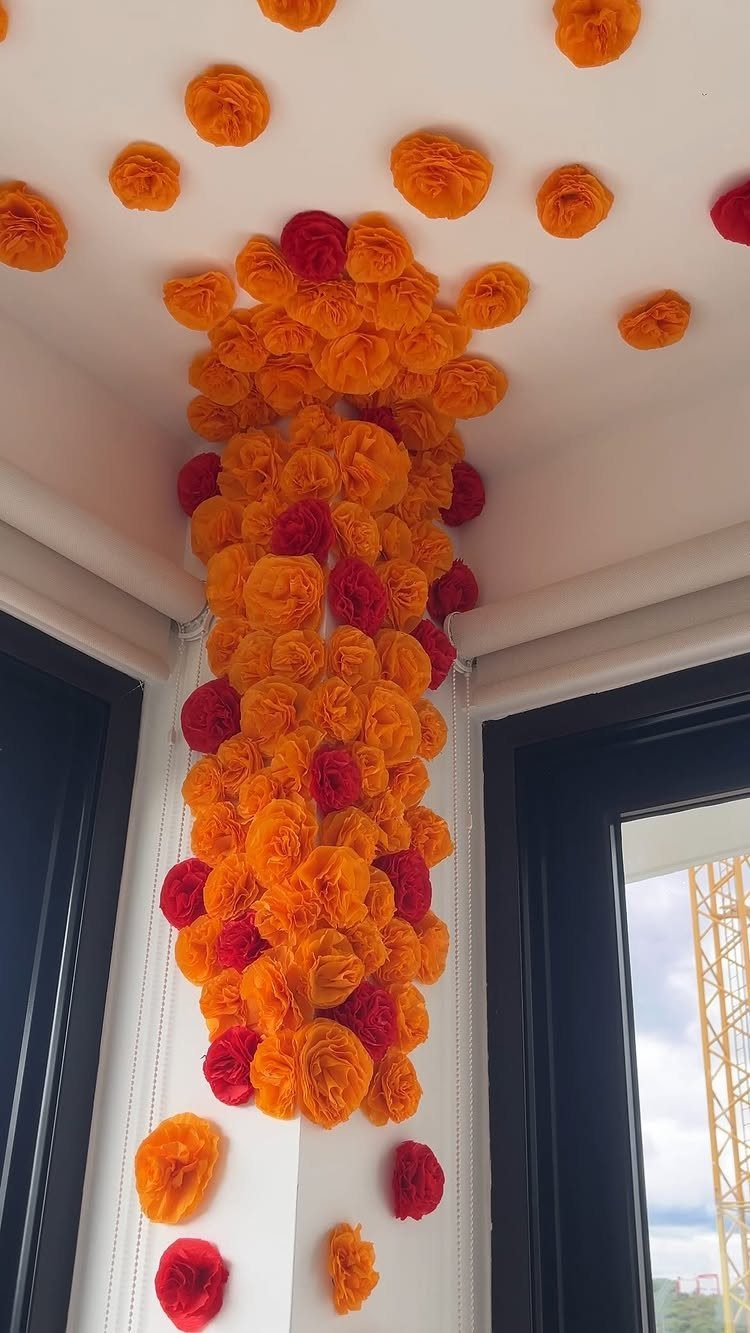 Orange and red paper pom-poms cascading down a white wall and ceiling.