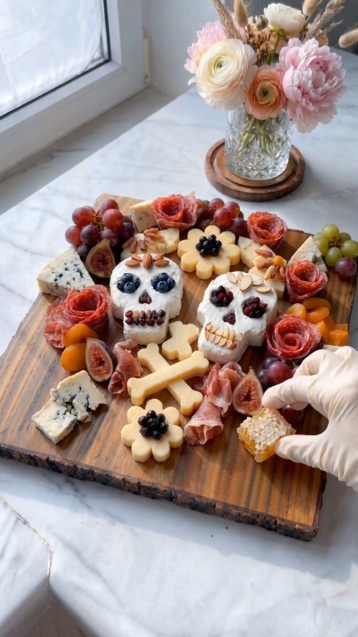 Cheese skulls and charcuterie platter arranged on a wooden board for Day of the Dead.