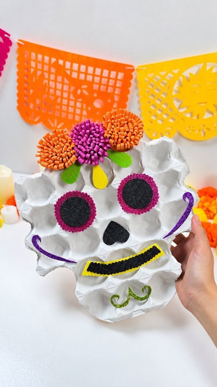 Egg carton sugar skull craft with colorful pom-poms and papel picado background