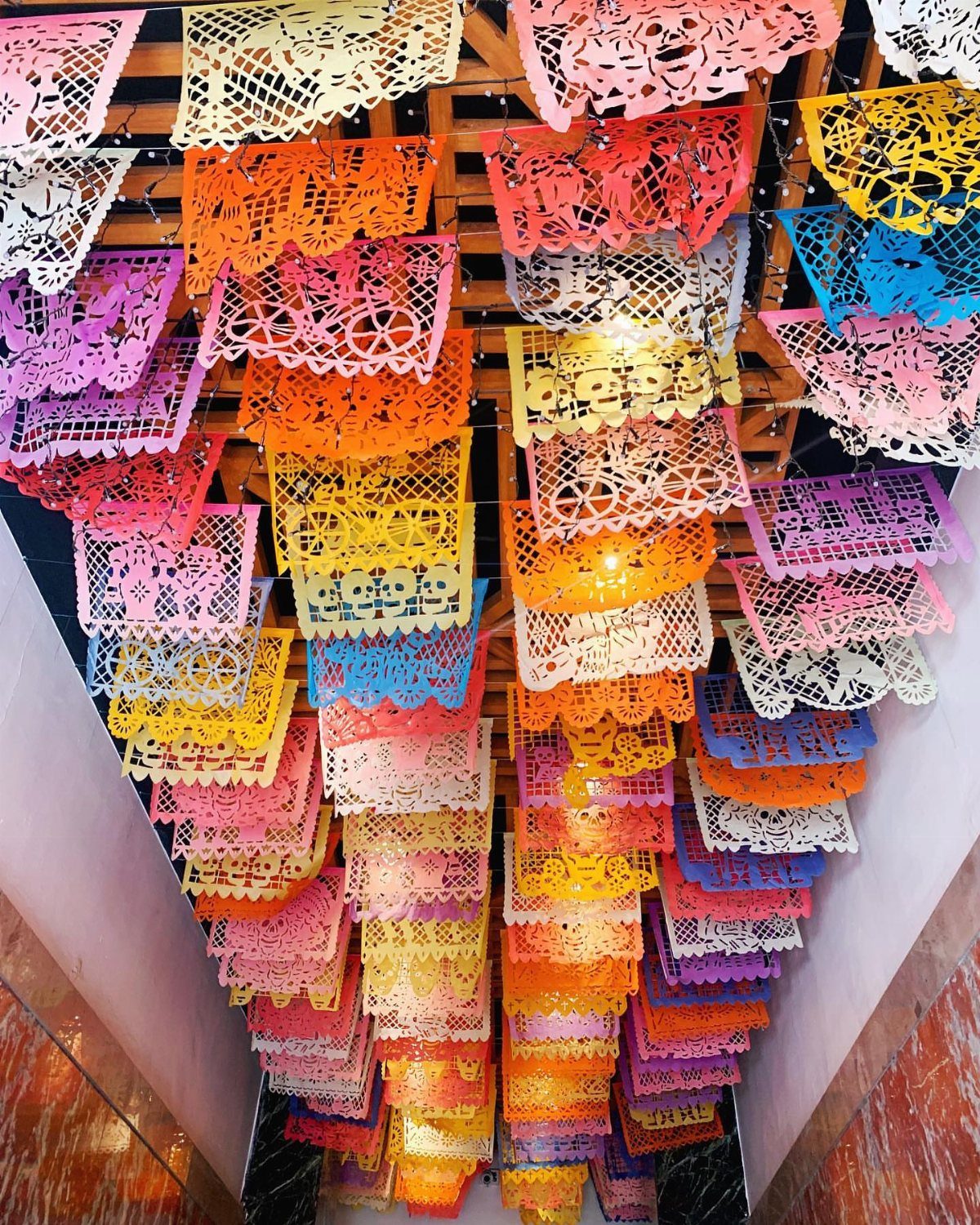 Colorful papel picado banners hanging from a wooden ceiling in a hallway.