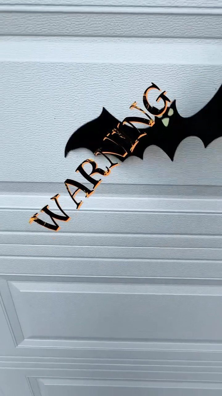 Black bat cutout with orange WARNING text on a white garage door
