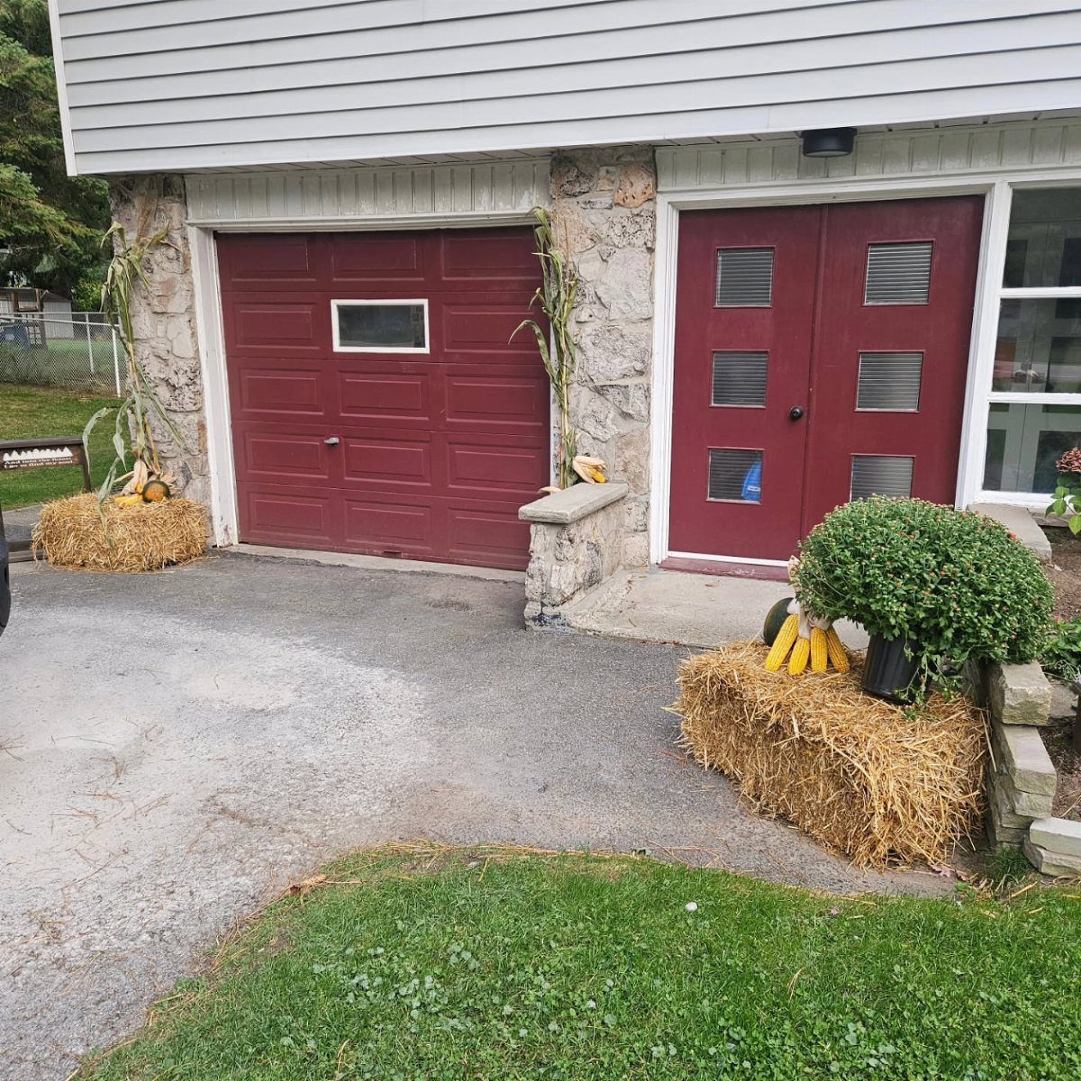 Red garage door decorated with hay bales, corn stalks, and pumpkins for autumn.