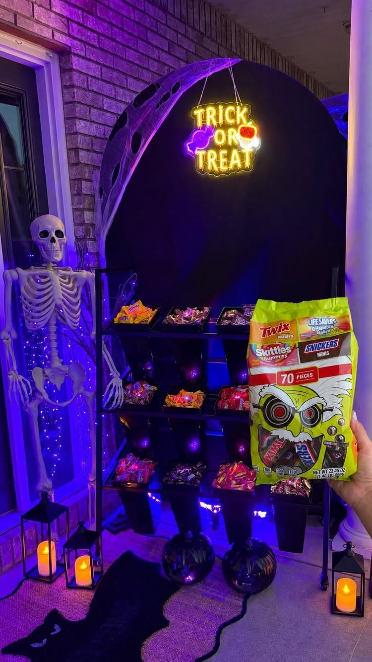 Halloween candy station with a skeleton, glowing sign, and purple lighting in a garage.