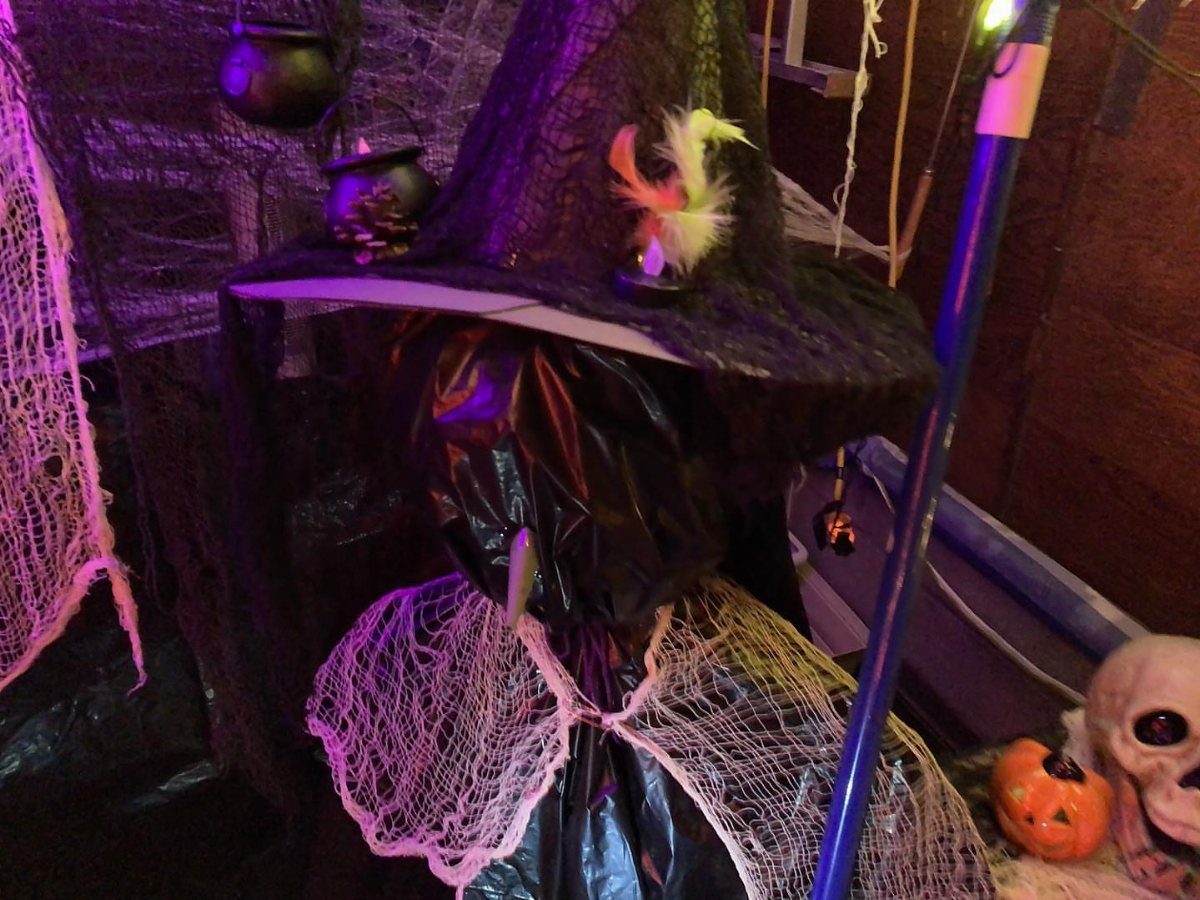 Witch figure with pointed hat and spiderwebs in a purple lit garage