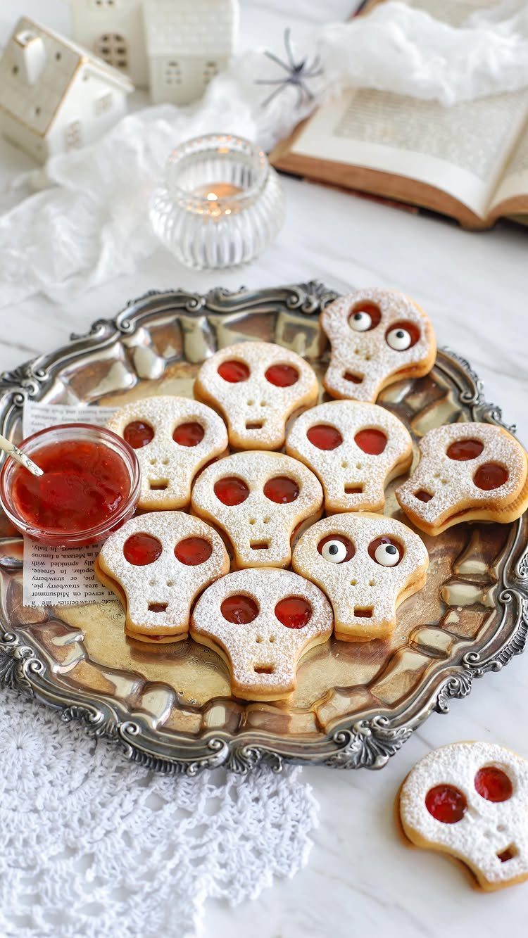 Skull-shaped sugar cookies with red jam eyes on an ornate silver platter.