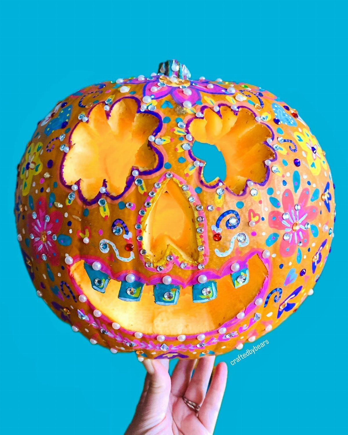 Carved orange pumpkin decorated as a colorful sugar skull with rhinestones and paint.