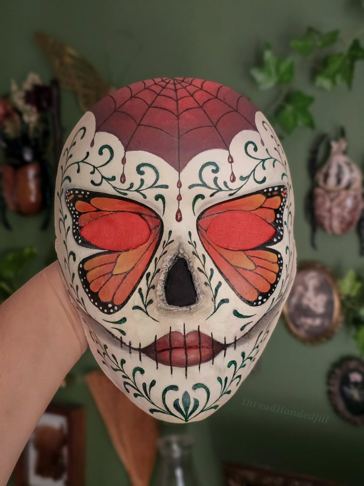 Painted sugar skull with monarch butterflies and a red spiderweb held by hand.