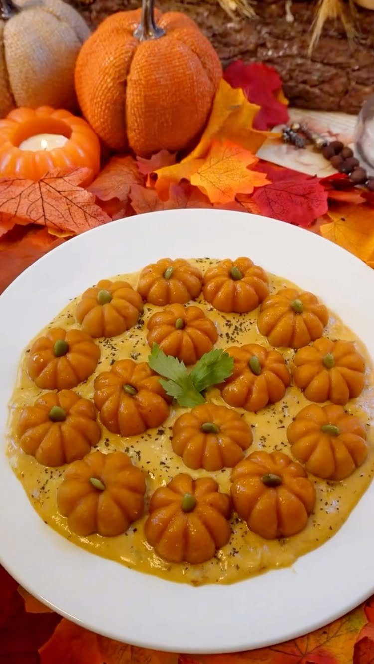 Pumpkin-shaped gnocchi in a creamy orange sauce on a white plate with autumn decor.