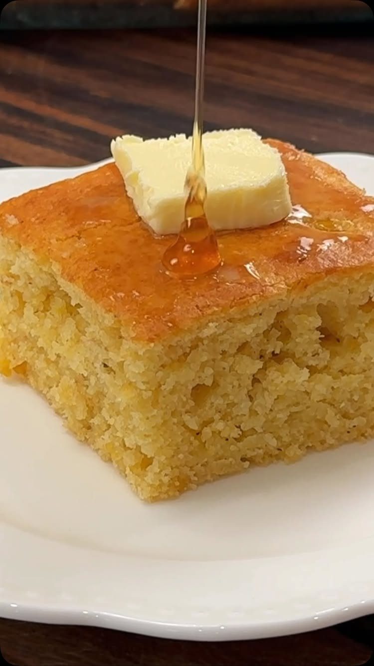Square piece of golden cornbread with melting butter and pouring honey on white plate