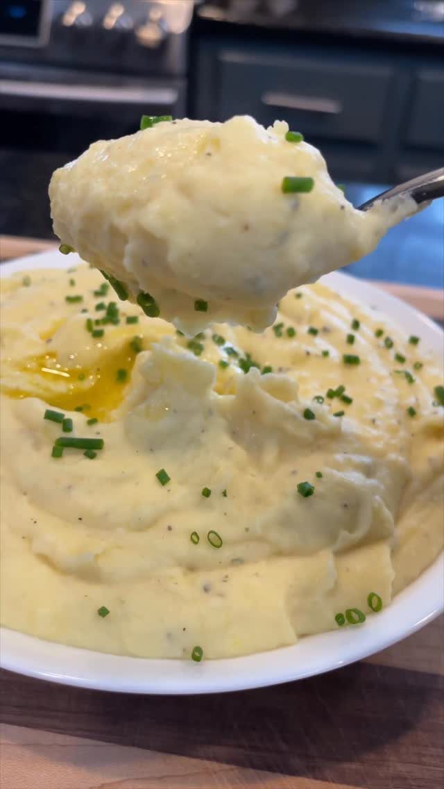 Mashed potatoes in a white bowl topped with melted butter and fresh chives.