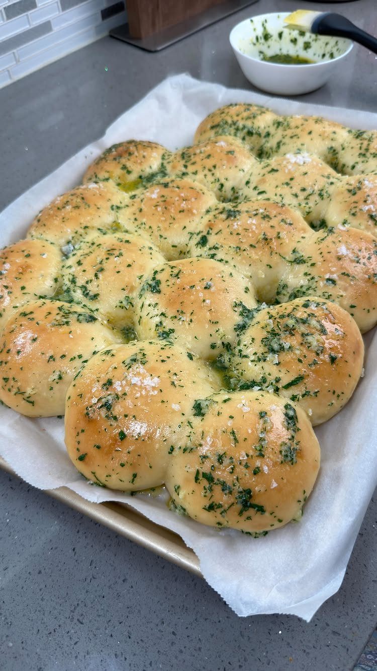 Garlic herb dinner rolls on a baking sheet topped with melted butter and parsley