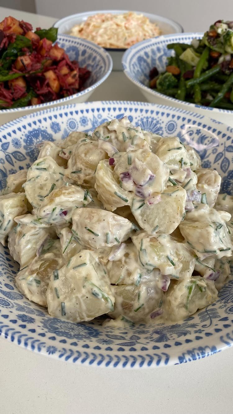 Creamy potato salad with red onion and herbs in a blue patterned bowl.